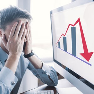 A man in distress holding his head in front of a computer screen displaying a graph, symbolizing business loss - Your Injury Law Group